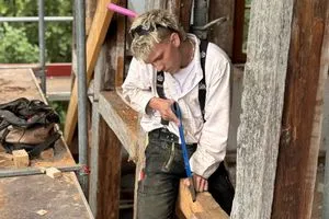 Auch der Auszubildende Leonhard packt kräftig mit an: Auf einem Balken sitzend macht er mit der Stoßaxt die Feinarbeit.